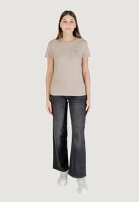 T-shirt beige a maniche corte, scollatura rotonda, leggero effetto texture, abbinato a jeans svasati grigio scuro e sneaker bianche. Logo sulla maglietta.
