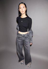 Schwarzes, kurz geschnittenes Langarmshirt mit gesticktem Logo, kombiniert mit hoch taillierten, weit geschnittenen grauen Jeans mit umgeschlagenem Saum und silbernen Schuhen.