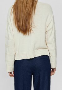 Maglione color crema a maglia con orlo a coste e maniche testurizzate, abbinato a pantaloni scuri. Il maglione ha una silhouette cropped rilassata.