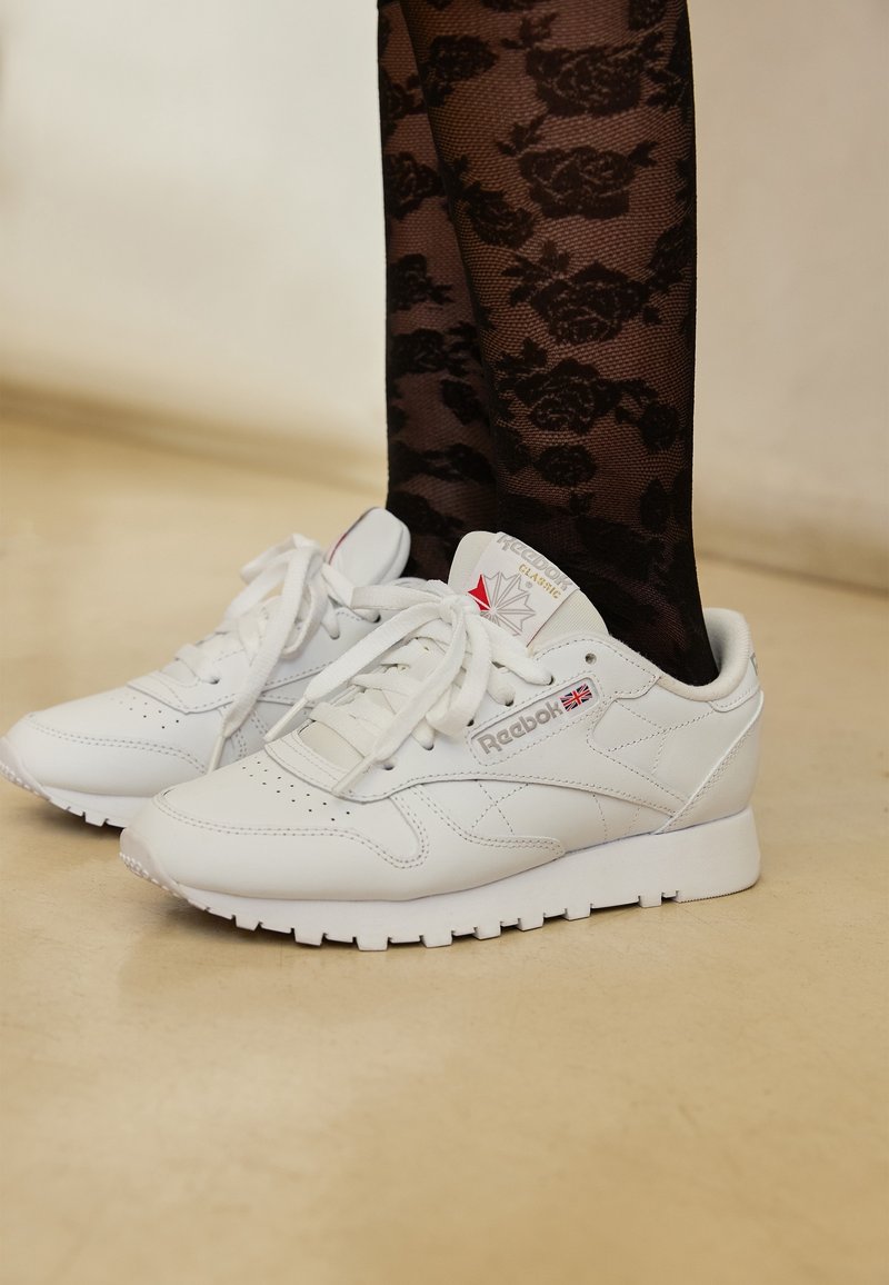 Vita läder Reebok sneakers med en slät yta, rund tå och perforeringar. Har en diskret logotyp och vit gummisula.