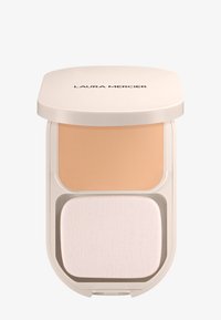 Base en polvo compacto con un tono beige claro en un estuche redondeado de color crema. Incluye una esponja aplicadora suave y blanca en la parte inferior.