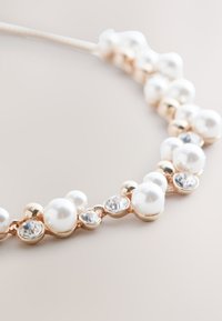 Pearl and crystal necklace featuring alternating white pearls and clear gemstones, set in a rose gold-tone metal chain. Smooth, glossy texture.