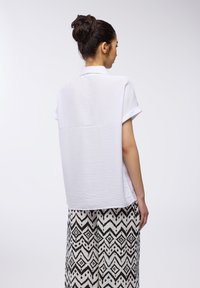Top bianco a maniche corte con una finitura testurizzata, abbinato a pantaloni larghi a righe bianche e nere caratterizzati da motivi a zigzag.