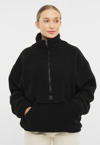 Čierny fleecový pulóver s vysokým golierom, predným zipsom a prednou vreckom. Má voľný strih a rebrované manžety pre pohodlnú textúru.