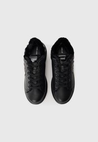 Fekete bőrből készült sneakers pár fekete fűzővel és puha szőrme béléssel, fémes KARL logóval a nyelvén és az oldalán.