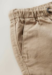 Shorts khaki realizzati in cotone morbido, con vita elastica, chiusura con cordoncino e tasca laterale con dettagli di cucitura visibili.