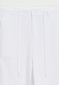Pantalons blancs à cordon de serrage avec une texture lisse, des plis à l'avant, une fermeture à bouton et des poches latérales pour plus de fonctionnalité.