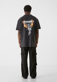 Sort oversized t-shirt med et grafisk print af en figur med ildfulde vinger på ryggen; parret med sorte cargo-bukser med sidelommer.