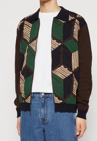 Stickad cardigan med dragkedja framtill, med ett geometriskt mönster i grön, brun och beige. Kontrast i marinblå krage och ribbad mudd.