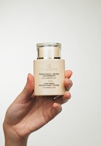 Bouteille en verre beige avec une bande dorée, étiquetée "Fond de teint et base Even Finish", dotée d'un capuchon transparent et d'un distributeur à piston.