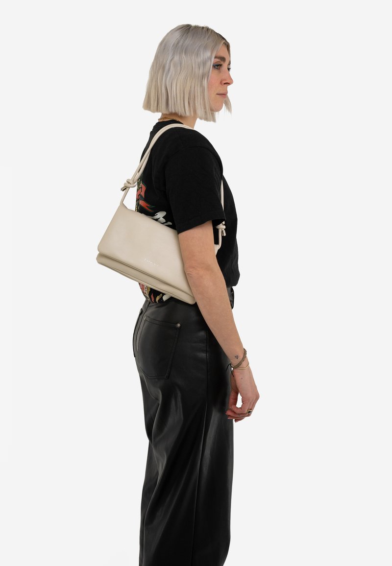 Krém színű táska texturált anyagból, elegáns, háromszög alakú dizájnnal, állítható pántokkal és minimalista logó részlettel.