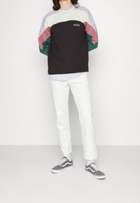 Felpa nera e multicolore con maniche di colore viola chiaro, rosa e verde; pantaloni bianchi; sneakers grigie; vestibilità casual; texture di tessuto morbida.