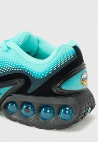 Turkoosi ja musta urheilukengän verkkokangasyläosa, teksturoitu koristeellinen yksityiskohta ja näkyvä ilmatyyny pohjassa. Varustettu mustalla kumipohjalla.