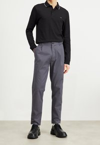 Black long-sleeve polo with white collar accents, paired with gray trousers and black lace-up shoes, highlighting a modern fit and clean lines.