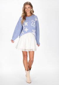 Ljusblå, oversized tröja med vit blommig broderi, i kombination med en vit kjol med spetskant och beige ankelskor.