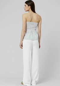 Top sans épaules à smocks rayé dans des couleurs claires, associé à un pantalon blanc à jambe larges. Texture lisse, coupe décontractée, embellissements minimaux.