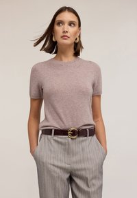 Svetle růžový pletený svetr s krátkým rukávem a kulatým výstřihem, doplněný šedými pruhovanými kalhotami a vínovým páskem se zlatou kulatou sponou.