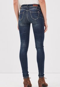 Mörkblå skinnyjeans med hög midja och bakfickor, med lätt blekning och en slät denimtextur. Bärs med bruna ankelstövlar.