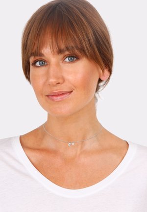 Silberne Choker-Halskette mit einem kleinen Halbmond-Anhänger und einem winzigen Edelstein, präsentiert auf einem schlichten weißen Oberteil.