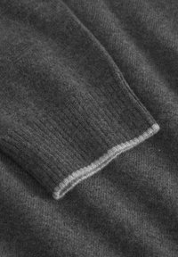 Nahaufnahme eines dunkelgrauen gestrickten Pulloverwärmers mit geripptem Bündchen und einem hellgrauen Kantenakzent.