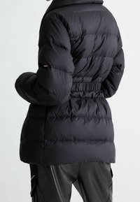 Sort pufferjakke med bælte i taljen, høj krave og quiltet design i skinnende, glat stof, ideel til koldt vejr.