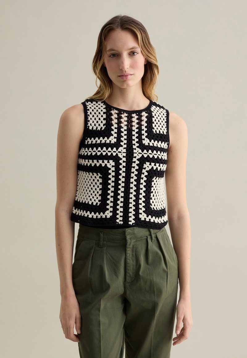 Top corto lavorato a maglia nero e crema con un motivo geometrico, senza maniche e tessuto testurizzato. Abbinato a pantaloni verde oliva.