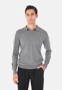 Maglione polo grigio a maniche lunghe con colletto piatto e polsini a costine, realizzato in tessuto morbido, abbinato a pantaloni neri dal taglio morbido.