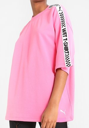 Personne portant un t-shirt ample rose Puma avec l'inscription « WET T-SHIRT » et une bande à carreaux sur l'épaule et la manche.