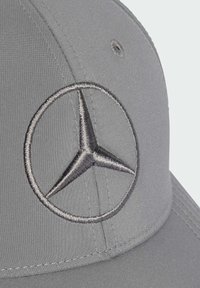 Nærbillede af en grå baseballkasket med et broderet sølvfarvet stjerne-logo med tre spidser på frontpanelet.