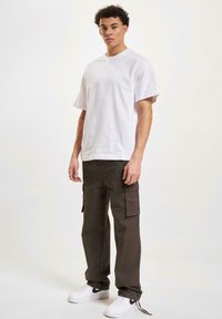 Camiseta de algodón blanca de manga corta, combinada con pantalones cargo verde oliva con bolsillos laterales, usados con zapatillas blancas.
