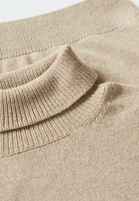Beige gerippter Strickrollkragenpullover mit umgeschlagenem Kragen, der die feine Wolletextur und Nähdetails zeigt.