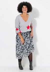 Maglione grigio con accenti a forma di stella rossa, abbinato a una gonne leopardata in bianco e nero. Gli stivali neri con borchie completano l'outfit.