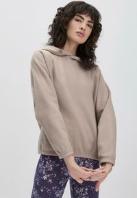 Felpa beige con cappuccio regolabile, spalle abbassate e polsini elasticizzati. Abbinata a leggings con motivo floreale in blu scuro.