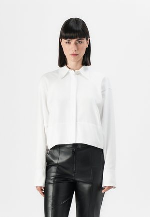 White cropped shirt with a button-down collar, long sleeves, and a textured fabric, paired with black leather pants featuring a zippered front.