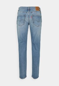 Ljusblå denimjeans med bakfickor och en brun läderlogotyp på midjebandet, visad bakifrån mot en vit bakgrund.