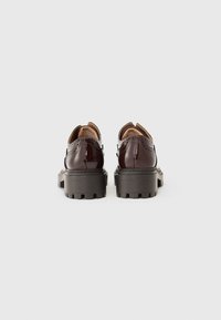 Bruna patenterade läderskor med brogue-detaljer, gummisula med klack och rund tå, med en polerad finish och sydda detaljer.