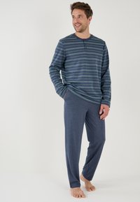 Gestreepte lange mouwen thermoshirt in marineblauw en groen met knoopdetails, gecombineerd met effen marineblauwe loungebroeken. Beide van zacht, ademend materiaal.
