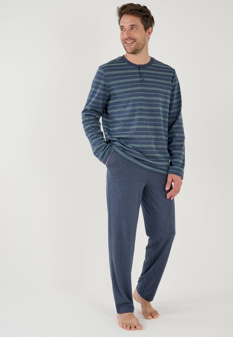 Gestreepte lange mouwen thermoshirt in marineblauw en groen met knoopdetails, gecombineerd met effen marineblauwe loungebroeken. Beide van zacht, ademend materiaal.