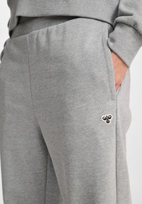 Graue Jogginghose aus weichem Material mit lockerem Schnitt, ausgestattet mit einer Seitentasche und einem kleinen gestickten Bienenlogo am Saum.