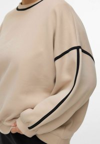 Beige sweatshirt met zwarte accenten, ruime pasvorm, ronde halslijn, lange mouwen met manchetten, zachte textuur en een minimalistisch ontwerp.