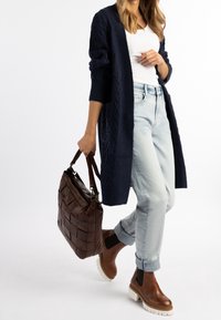 Granatowy dzianinowy sweter rozpinany, biały top, jasne dżinsy, brązowe skórzane botki za kostkę z białymi podeszwami oraz ciemnobrązowa pleciona torebka.