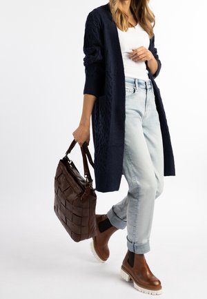Granatowy dzianinowy sweter rozpinany, biały top, jasne dżinsy, brązowe skórzane botki za kostkę z białymi podeszwami oraz ciemnobrązowa pleciona torebka.