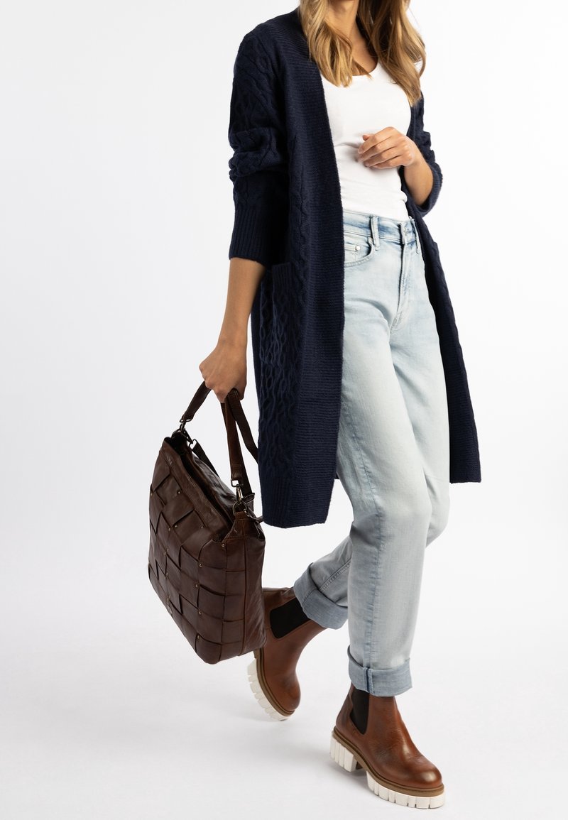 Granatowy dzianinowy sweter rozpinany, biały top, jasne dżinsy, brązowe skórzane botki za kostkę z białymi podeszwami oraz ciemnobrązowa pleciona torebka.