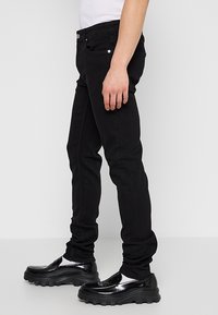 Jeans negros ajustados de mezclilla, con una textura suave, diseño estándar de cinco bolsillos y combinados con zapatos negros gruesos.