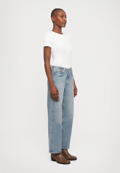 White fitted t-shirt, light blue wide-leg jeans, and brown heeled boots. Jeans feature a classic five-pocket design and subtle fading.