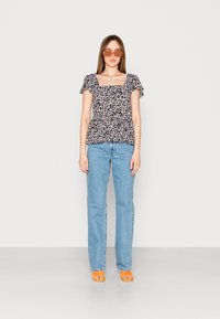 Top peplum floral com decote quadrado e mangas franzidas; jeans azuis; sandálias laranja; modelo a usar óculos de sol laranja. Fundo simples.