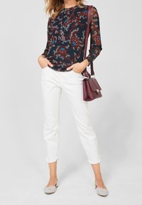 Svart långärmad blus med färgglad blommönster, matchad med vita kapade byxor och ljusgrå flats; bordeauxfärgad handväska med axelrem.