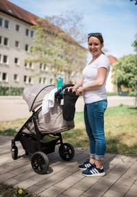Grijze kinderwagen met een zwart frame, stoffen zitting en grote wielen. Een blauwe waterfles en een zwarte accessoire tas zijn aan de handgreep bevestigd.