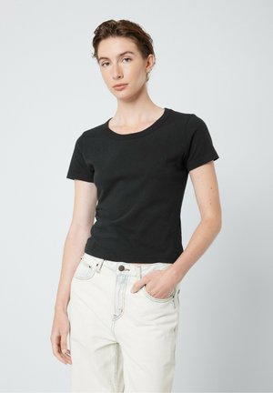 T-shirt noir en coton à manches courtes, col rond, design ajusté. Associé à un jean clair taille haute. Texture unie, sans motifs.