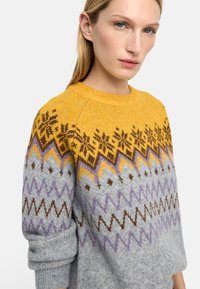 Sweter dziergany na drutach z żółtą, wzorzystą górą z motywami płatków śniegu i zygzaków, przechodzącą w jasnoszare ciało. Przytulna tekstura.